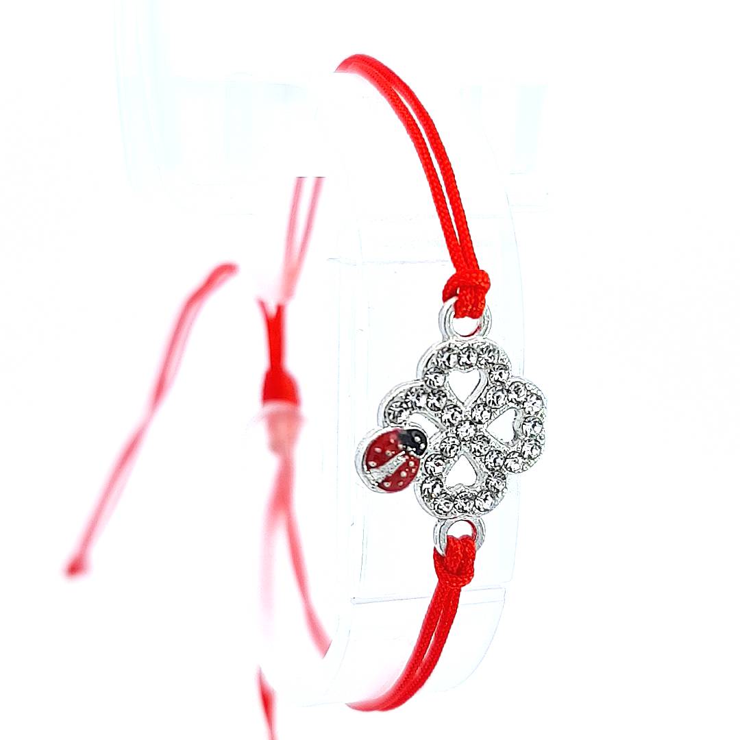 The 'Ladybird Luck Clover' Martisor Bracelet presented on a stand, highlighting the detailed crystal clover charm and the vibrant red cord against a pristine white backdrop.