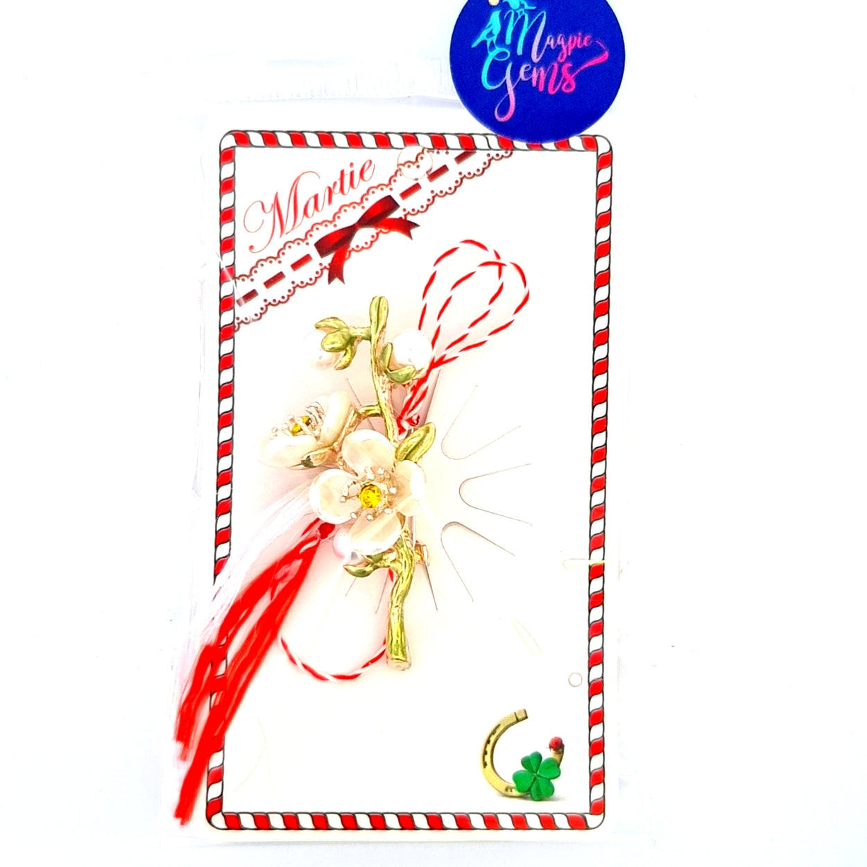 Ivory Cherry Blossom Martisor Brooch displayed on a decorative card with red and white accents, featuring delicate ivory cherry blossoms with golden details and the traditional red and white Martisor bow, symbolising spring and renewal. Packaged in signature Magpie Gems clear bag.