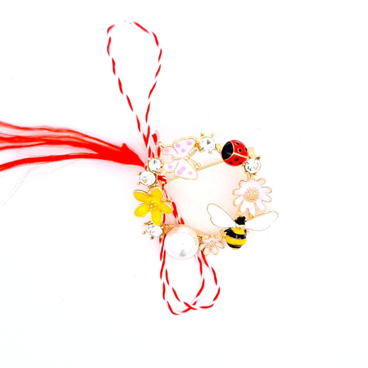 Spring Garden Martisor Brooch on a white background, featuring a circular design adorned with enamelled flowers, a bee, a ladybird, a butterfly, sparkling crystals, and a central pearl, paired with the traditional red and white Martisor bow to symbolise spring and vitality.