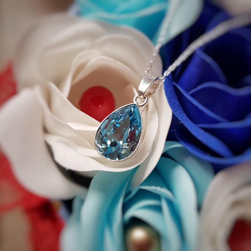 Close-up of the Aquamarine Blue Teardrop Pendant in Sterling Silver on a bed of roses.