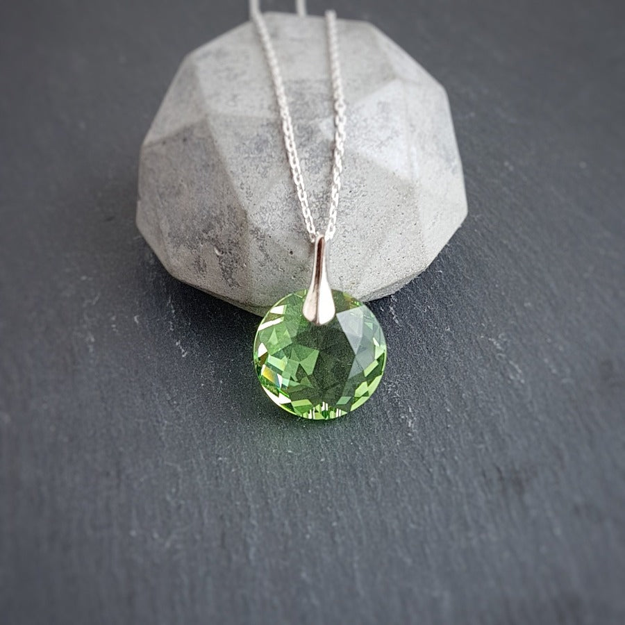 Peridot crystal pendant on a sterling silver chain, displayed against a geometric concrete background.