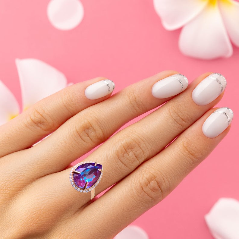 Woman's Hand with Handcrafted Rose Gold-Plated Sterling Silver Ring with a Pear-Shaped Crystal and Halo on Pink Background